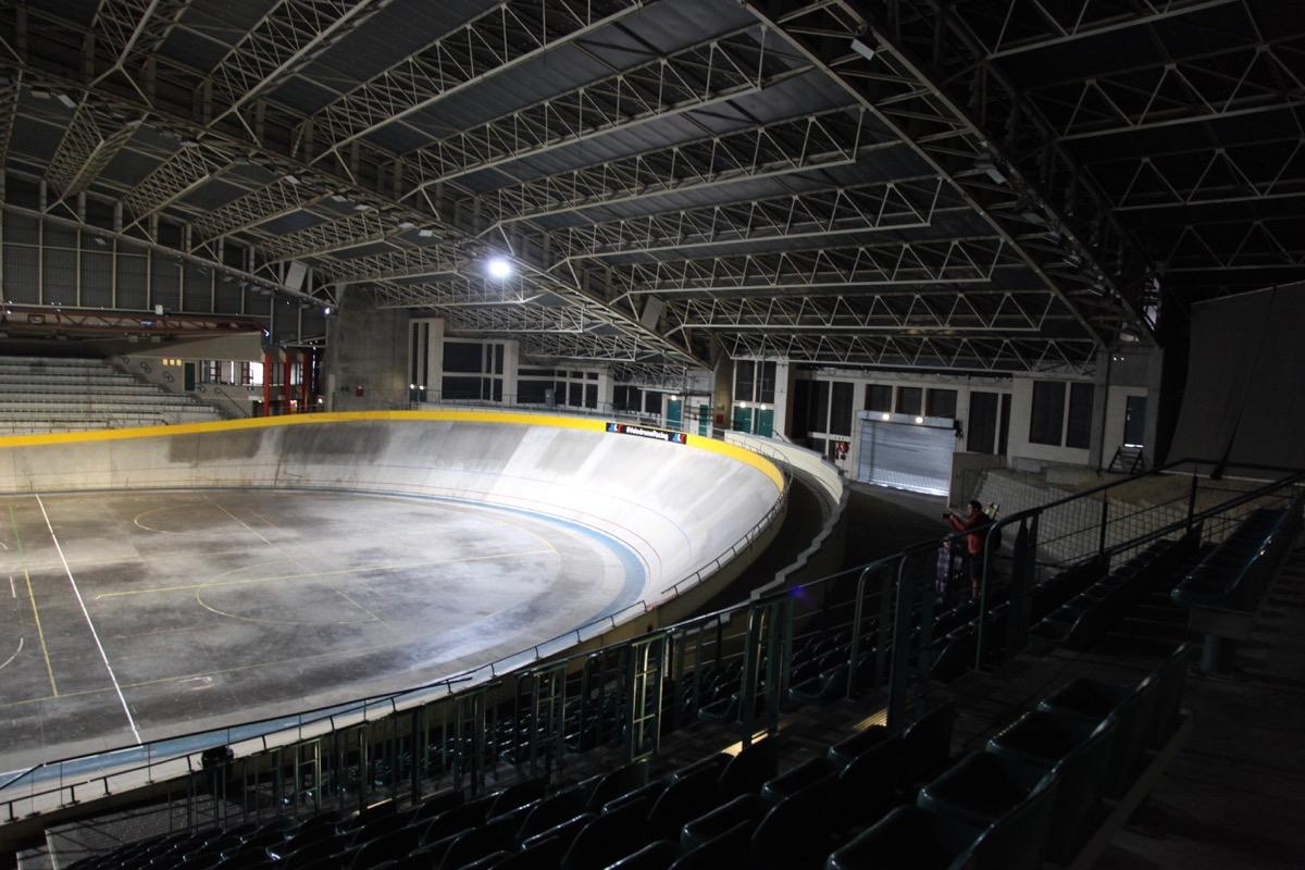 Empty 250-metre velodrome track bowl under arena lights, banked turns and yellow rail