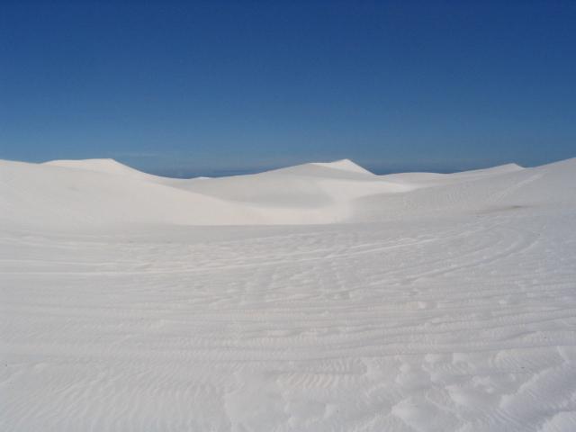 White dunes of the Atlantis dunefield rolling to a bare horizon under blue sky
