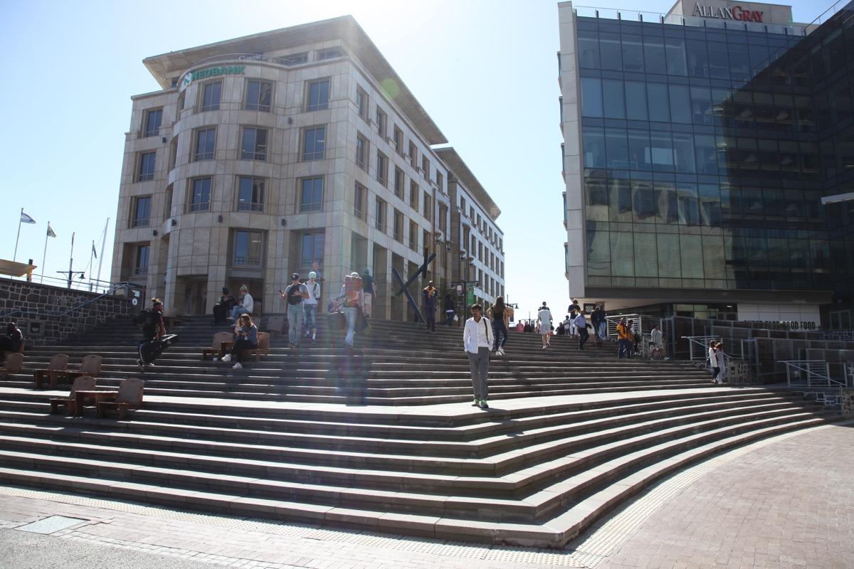 Wide stepped plaza between stone and glass buildings in hard sun