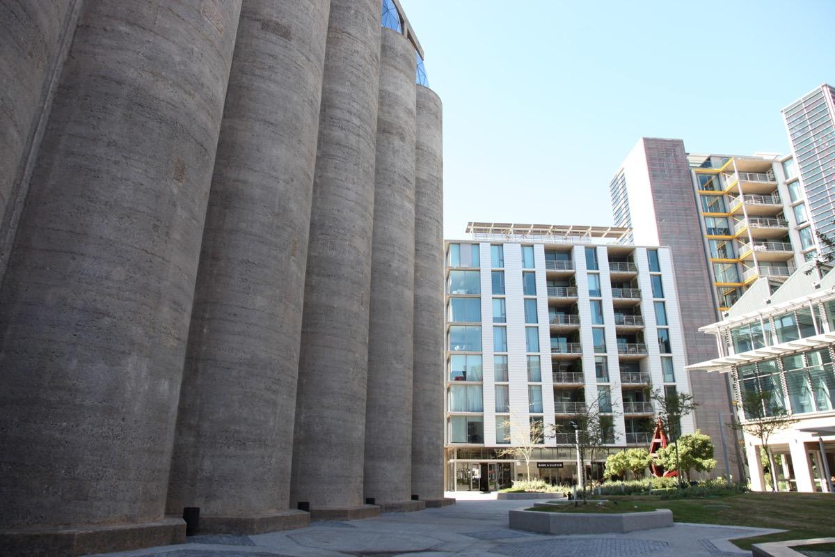 Raw concrete silo bins rising beside a modern apartment block