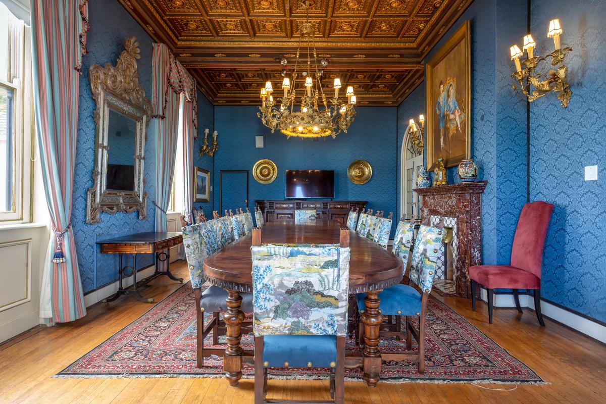Dining room with deep blue walls, gilt-coffered ceiling and a long laid table