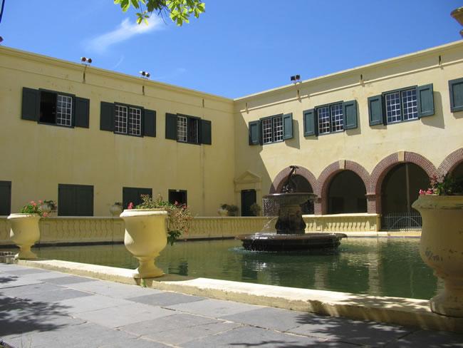 Yellow-walled courtyard with colonnade, urns and a long reflecting pool