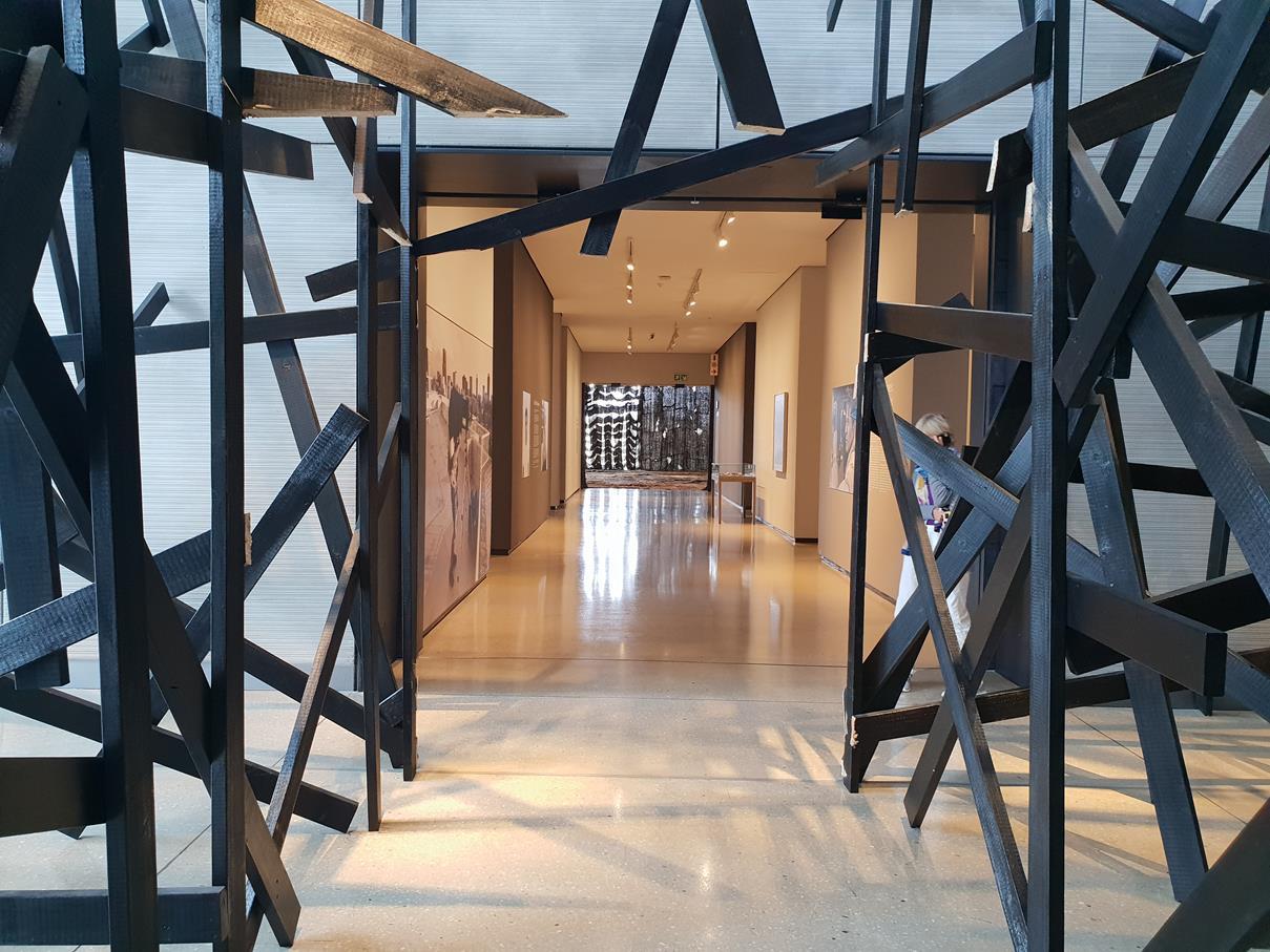 Corridor seen through a lattice of black steel beams inside the gallery