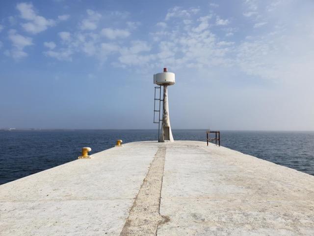 Concrete breakwater pier receding toward the sea with bollards and a beacon