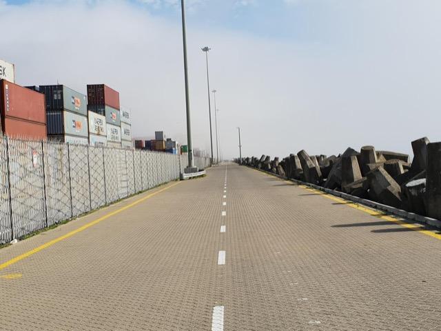 Breakwater service road lined with container stacks on one side and dolosse on the other