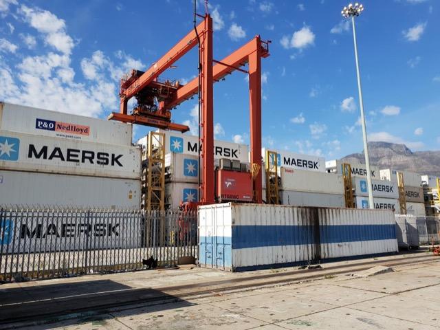 Red gantry crane over walls of stacked shipping containers under a blue sky