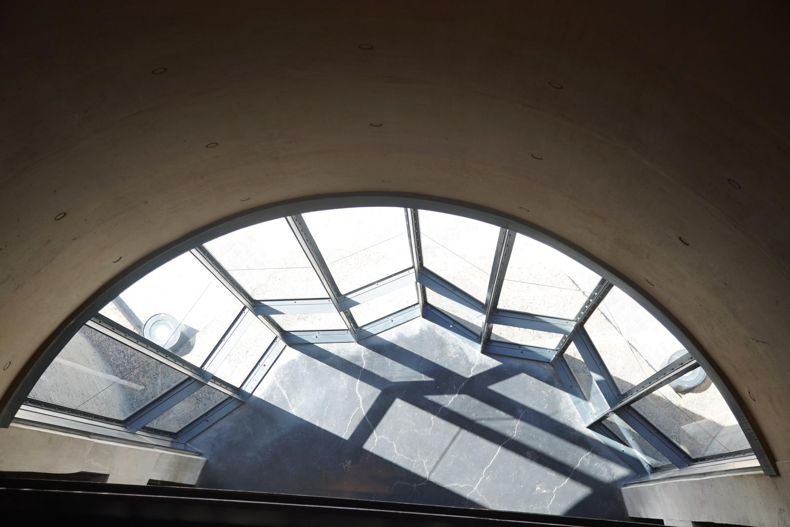 Arched skylight window set into raw concrete at the top of the silo